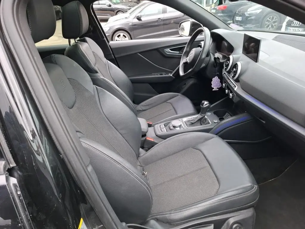 Vue intérieure côté conducteur de l'Audi Q2 noire 2023, sièges sport noirs et tableau de bord avec écran central.