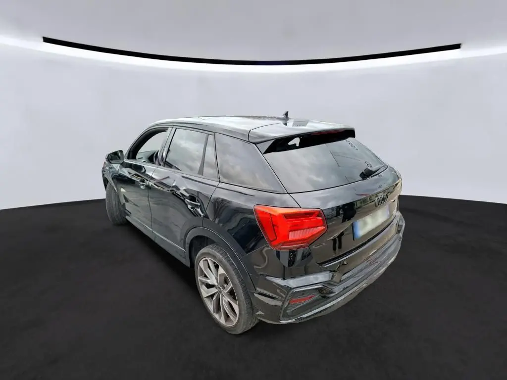 Audi Q2 noir vue 3/4 arrière droit, jantes alu et feux arrière LED dans un studio blanc.
