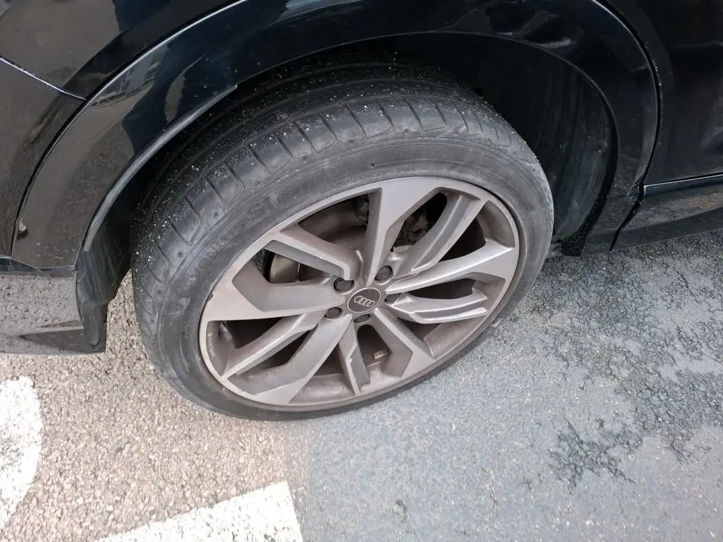 Gros plan sur la roue avant droite avec jante alu grise de l'Audi Q2 noire, version S-Line + 2023.