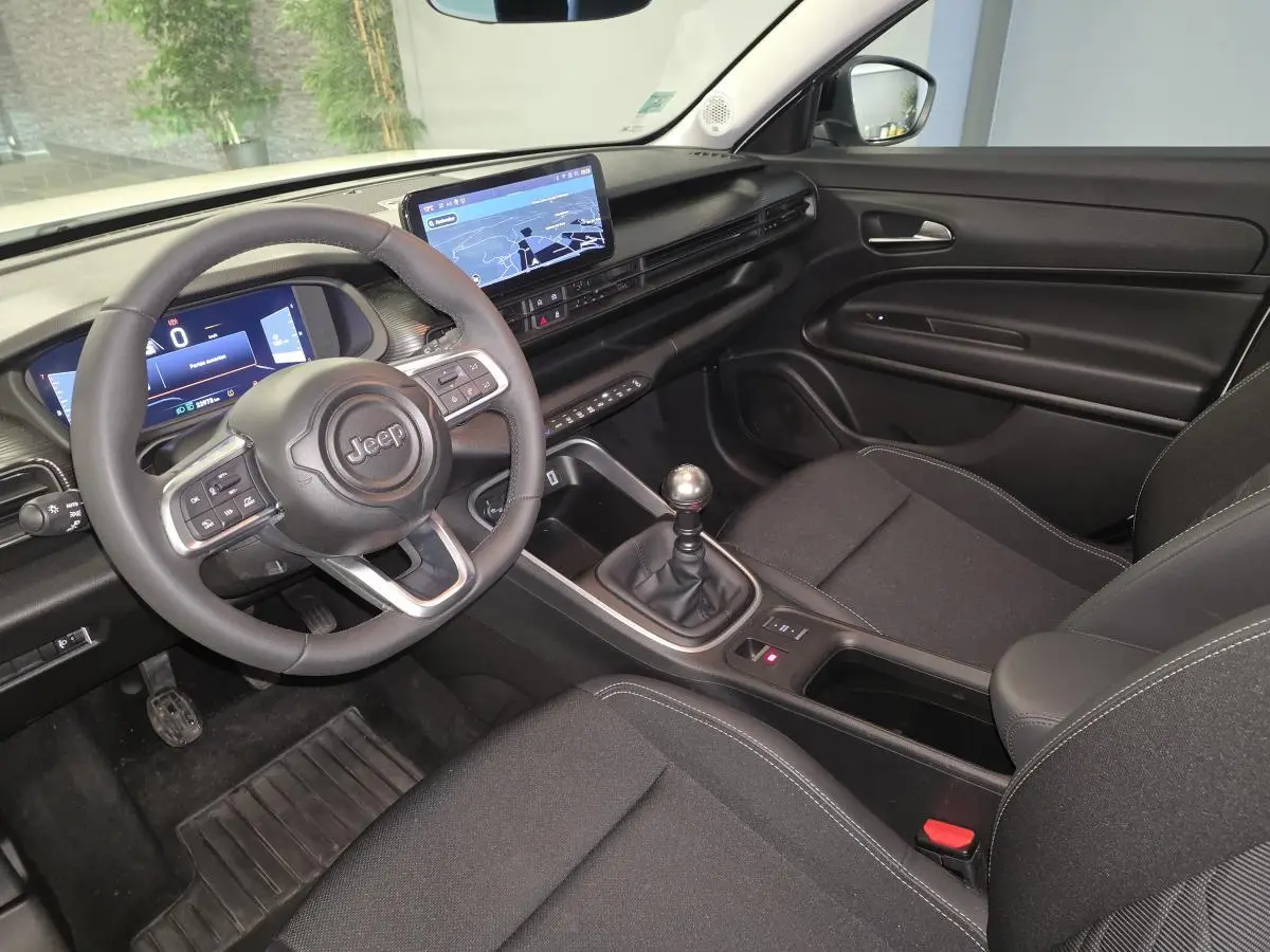 Vue intérieure côté conducteur du Jeep Avenger 2025, volant multifonction, tableau de bord numérique et levier de vitesses manuel.