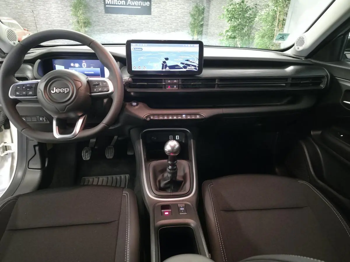 Vue intérieure avant du Jeep Avenger blanc 2025, volant multifonction, écran tactile central et levier de vitesses manuel.