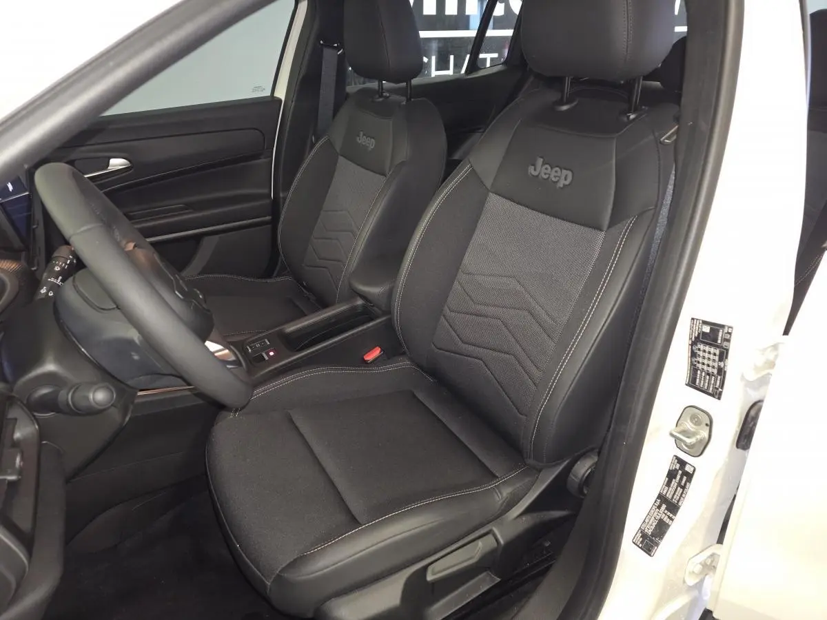 Vue intérieure côté conducteur du Jeep Avenger blanc 2025, sièges noirs mixte tissu/TEP avec logo Jeep brodé.