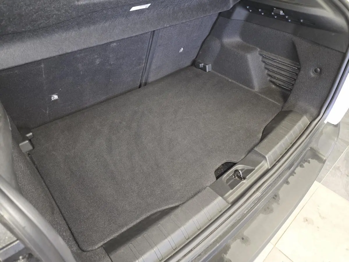 Vue rapprochée du coffre ouvert d'un Jeep Avenger blanc, montrant le tapis de sol noir et les finitions intérieures.