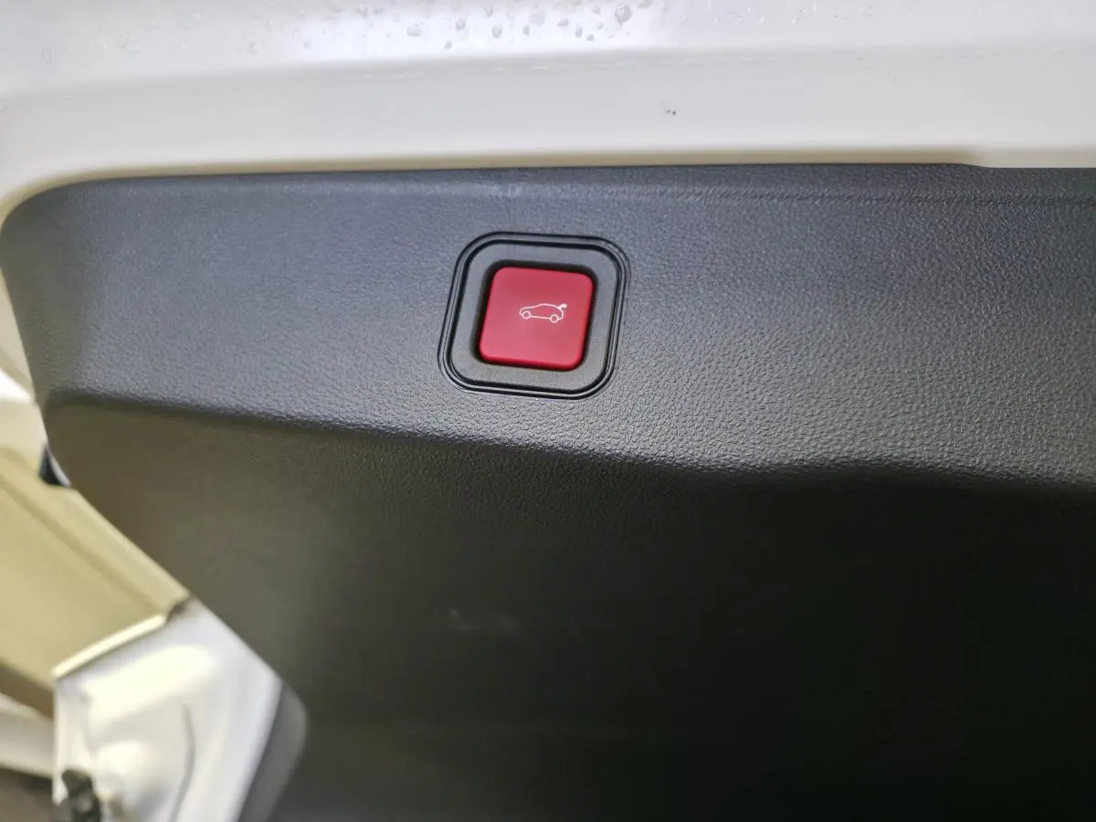 Gros plan sur le bouton rouge d'ouverture électrique mains libres du hayon d'un Jeep Avenger blanc 2025.