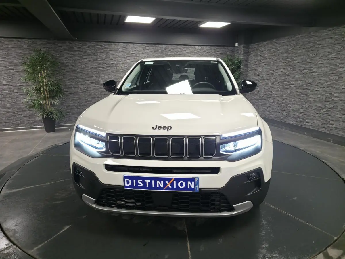 Vue de face du Jeep Avenger blanc avec phares LED allumés et calandre noire distinctive en showroom.