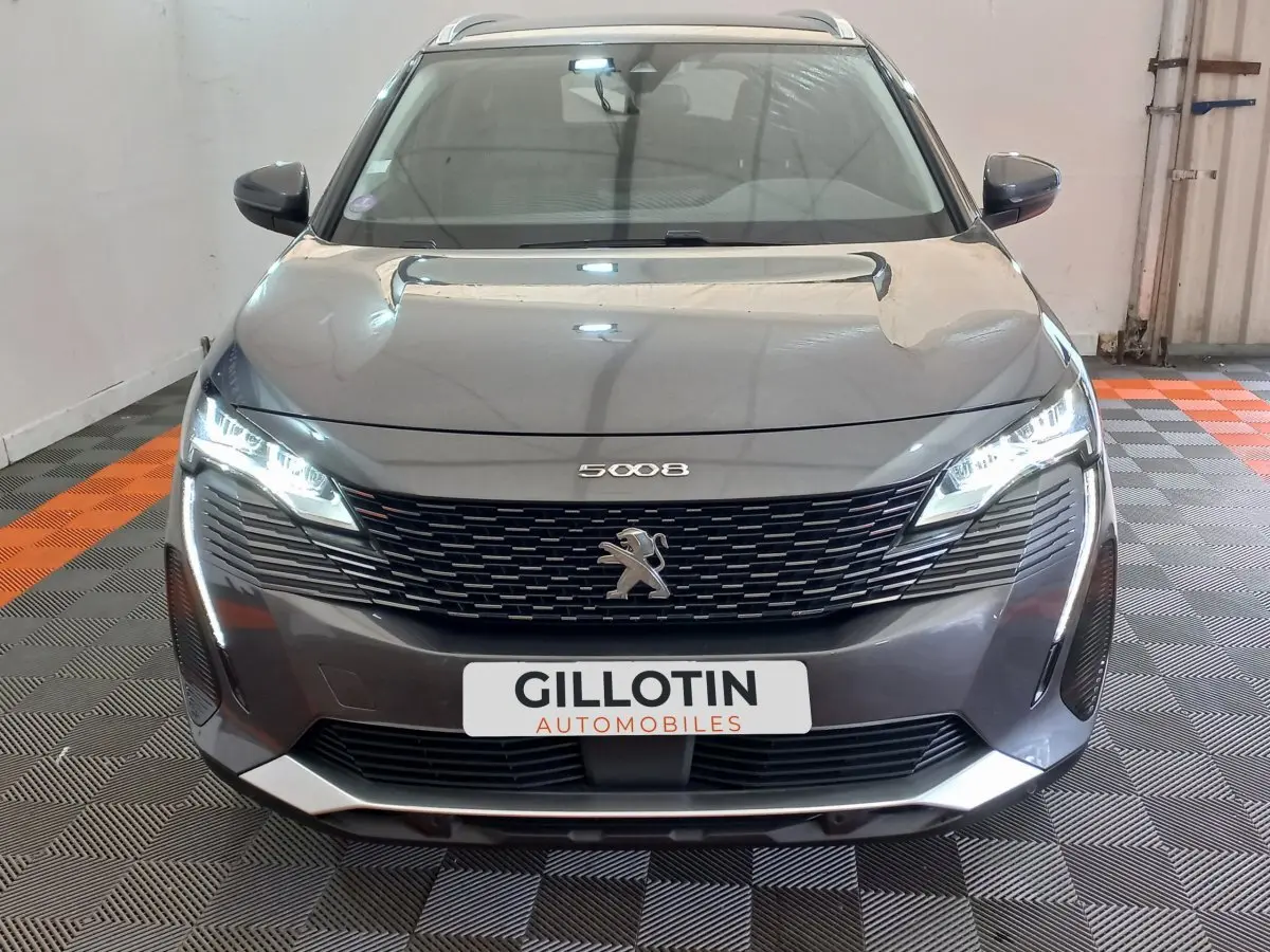 Vue frontale d'un Peugeot 5008 gris foncé avec phares LED allumés et calandre noire distinctive.