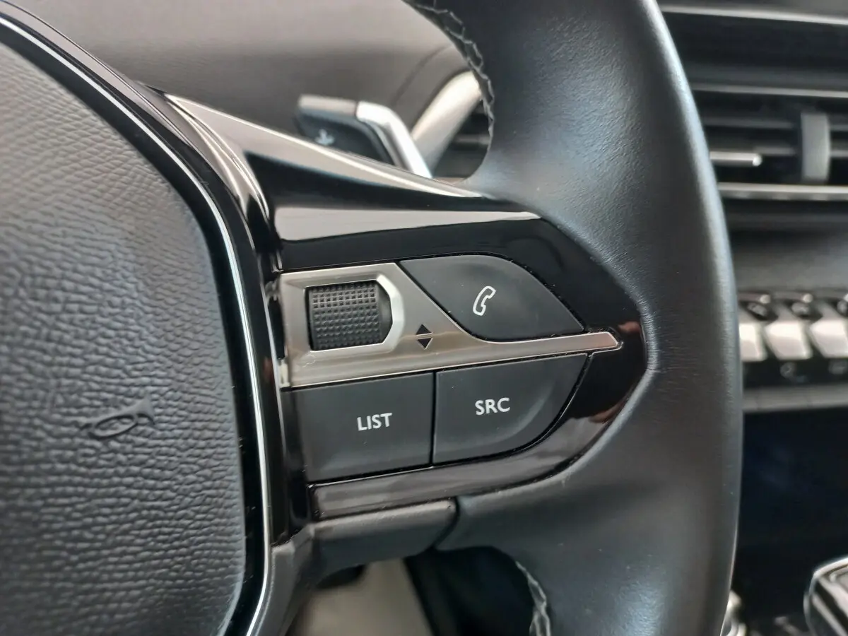 Gros plan sur les commandes gauche du volant cuir noir du Peugeot 5008 gris foncé, avec boutons LIST et SRC visibles.