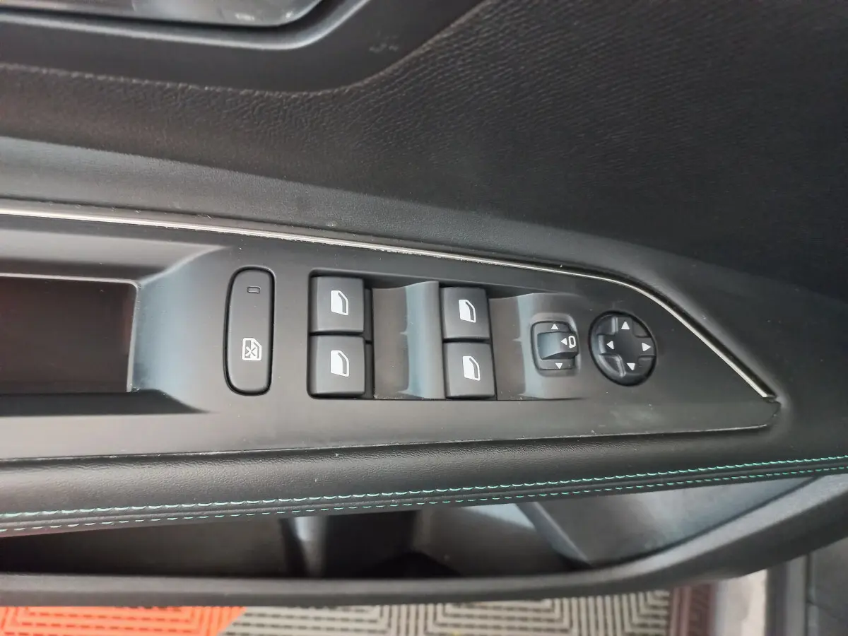 Panneau de porte côté conducteur noir avec commandes électriques des vitres et réglage des rétroviseurs sur Peugeot 5008 gris foncé.