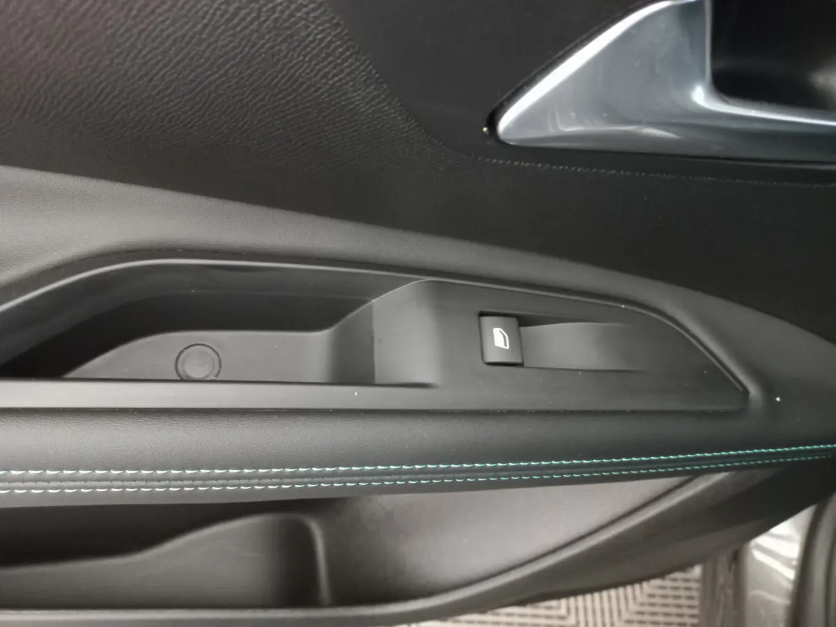 Gros plan sur la commande de lève-vitre côté gauche du Peugeot 5008 gris foncé avec surpiqûres bleues sur la porte.