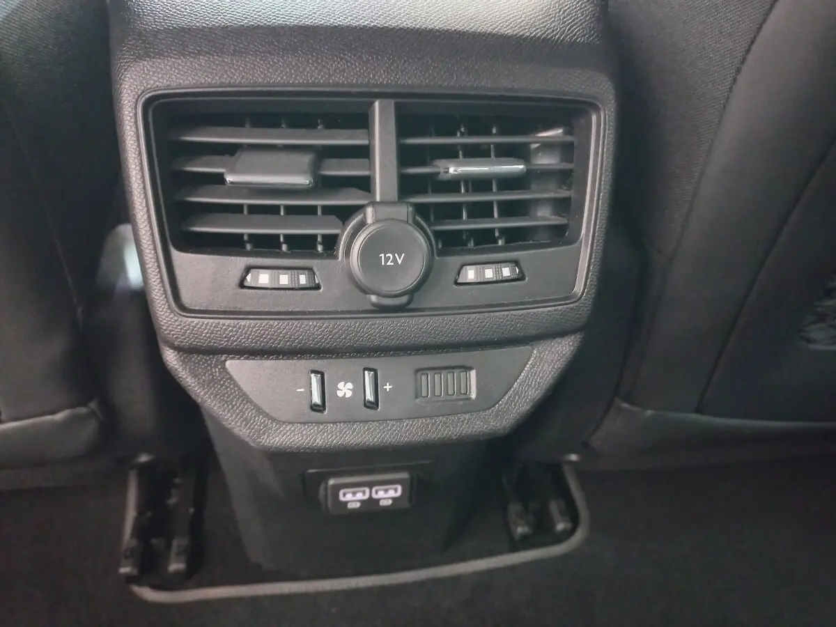Gros plan sur la console arrière noire du Peugeot 5008 2021 avec prise 12V, commandes ventilation et ports USB visibles.