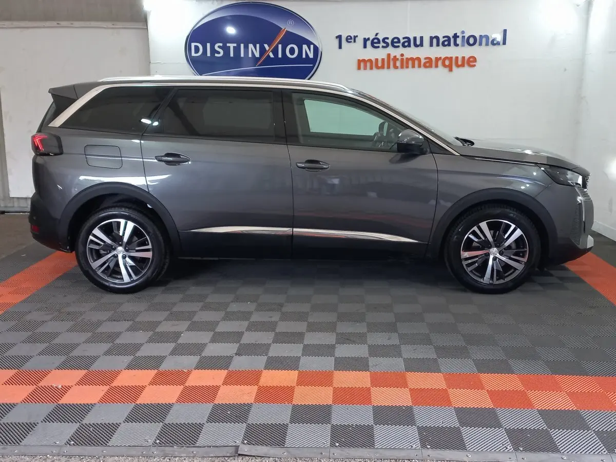 Profil droit d'un Peugeot 5008 gris foncé 2021 dans un showroom avec logo Distinxion en arrière-plan.