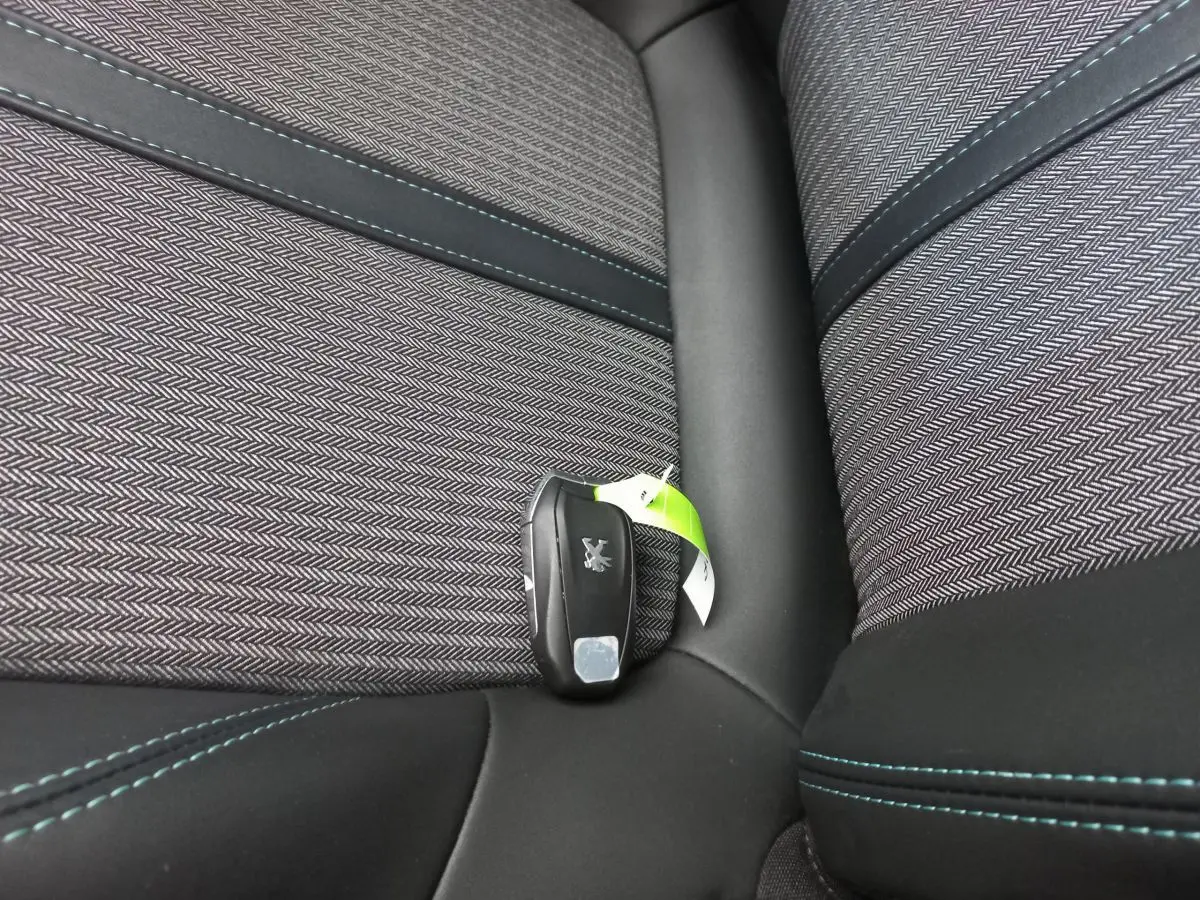 Clé Peugeot posée sur un siège tissu gris foncé avec surpiqûres bleues dans l'habitacle du 5008 Allure Pack.