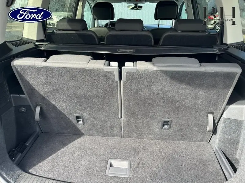 Vue arrière du coffre avec sièges rabattus d'un Volkswagen Touran 1.5 TSI Reflet d'Argent Métallisée, intérieur sombre.