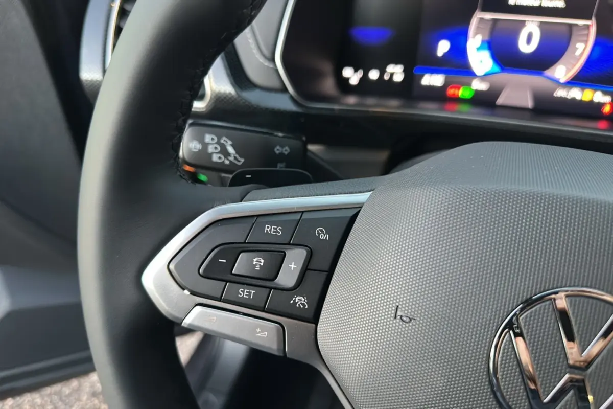 Gros plan sur le volant cuir multifonctions gris du Volkswagen T-Cross 2025 avec commandes de régulateur adaptatif.