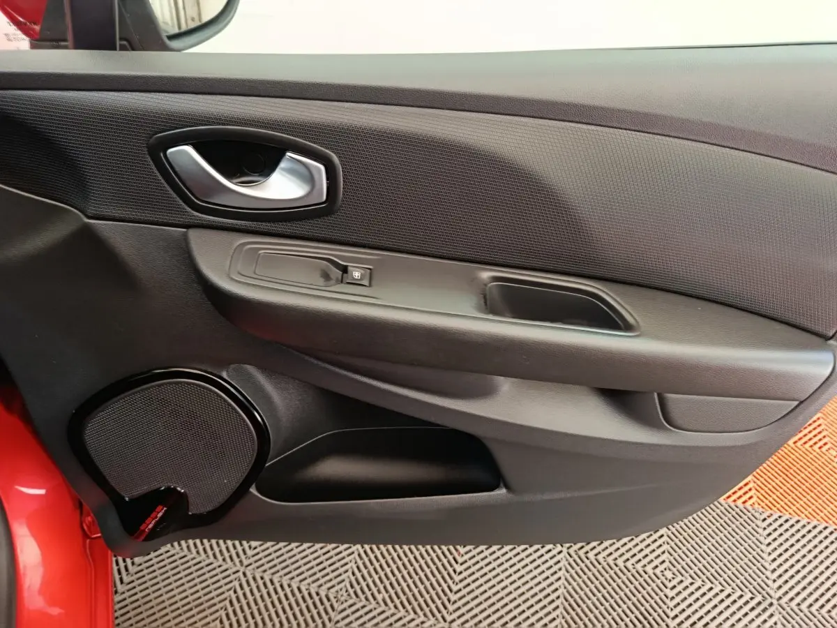 Détail de la porte intérieure côté conducteur de la Renault Clio rouge, avec poignée argentée et haut-parleur intégré.