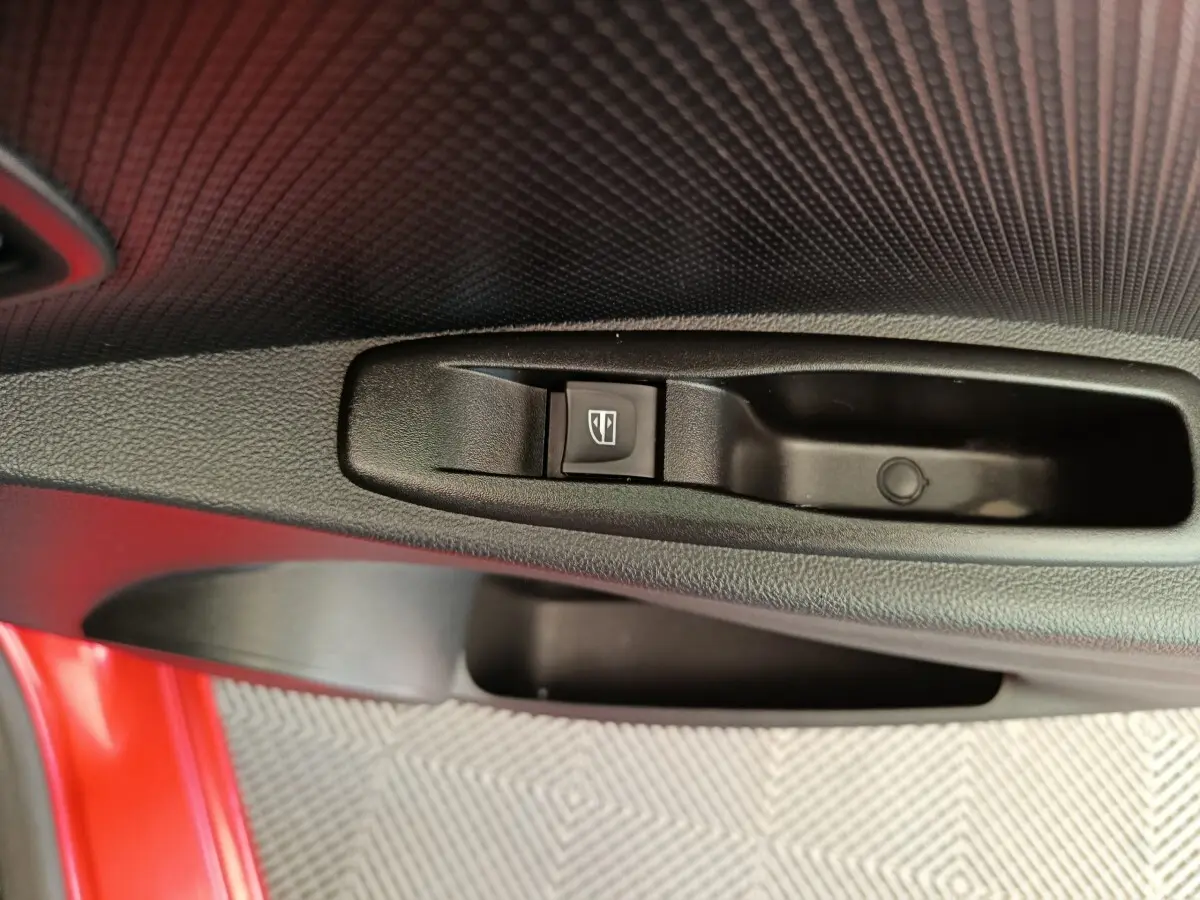 Gros plan sur la commande de lève-vitre côté conducteur d’une Renault Clio Intens rouge, intérieur noir texturé.