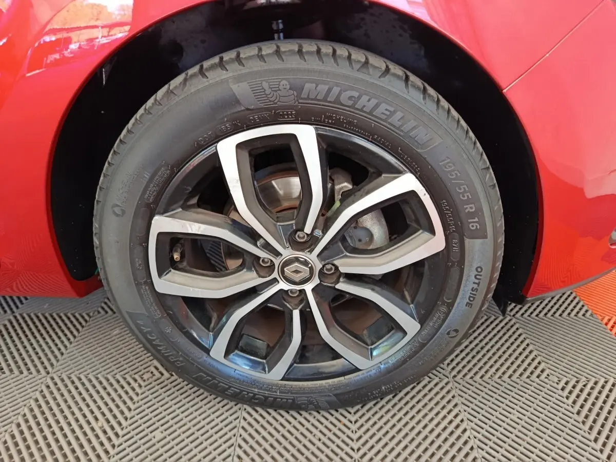 Gros plan sur la roue avant droite d'une Renault Clio rouge, jante alliage noire et argent avec logo Renault central.