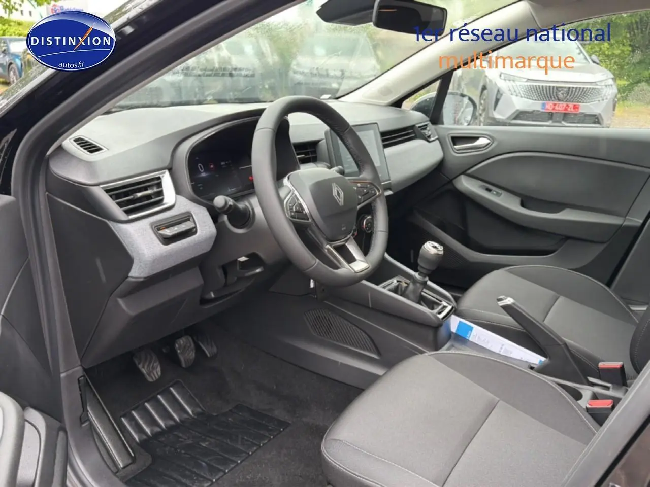 Intérieur avant droit de la Renault Clio V noire 2026, volant multifonction, écran tactile et boîte manuelle visibles.