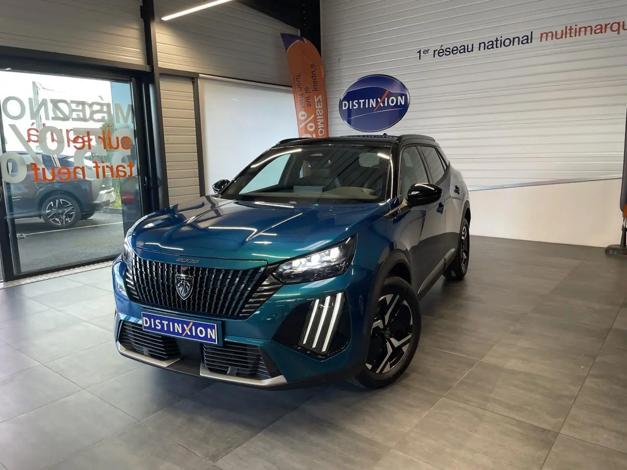 Peugeot 2008 bleu 3/4 avant droit en showroom, avec calandre noire et feux LED à griffes distinctifs.