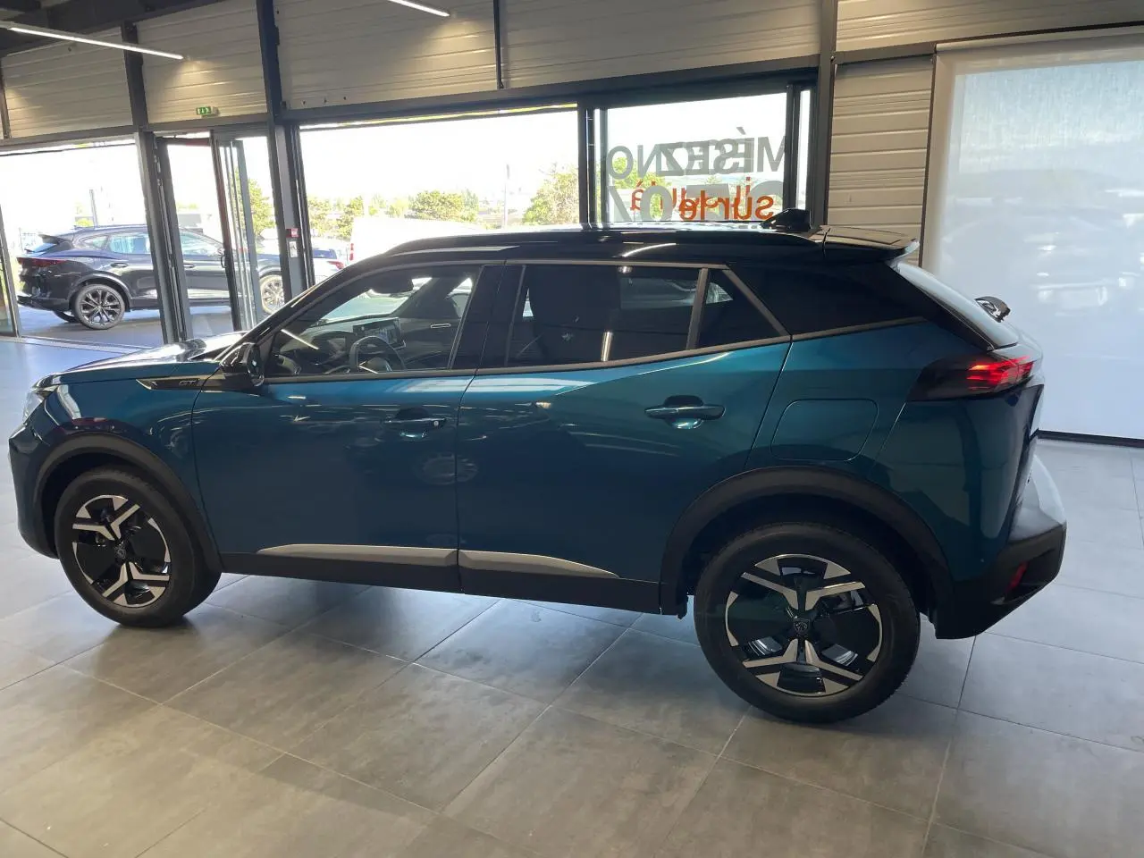 Peugeot 2008 hybride bleu vue de profil côté gauche, toit noir et jantes bicolores en concession.