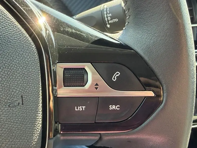Gros plan sur les commandes audio au volant du Peugeot 208 blanc Okénite, avec molette et boutons LIST, SRC, téléphone.