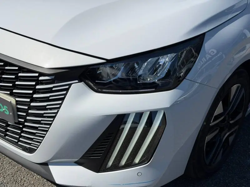 Gros plan sur l'avant droit blanc Okénite d'une Peugeot 208 1.2 100ch avec phares LED et calandre distinctive.