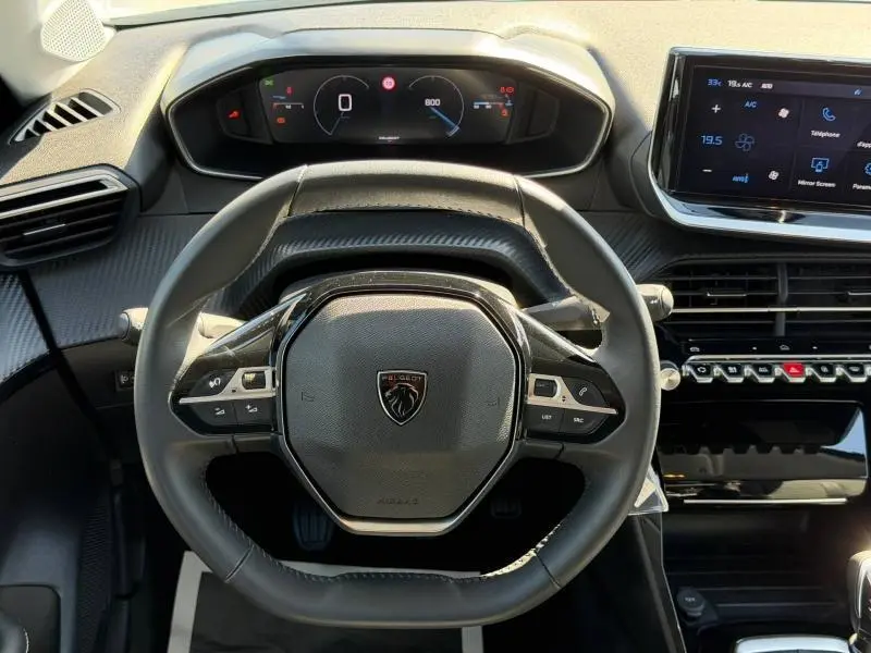 Vue rapprochée du volant multifonction noir et du tableau de bord numérique de la Peugeot 208 blanche 2025.