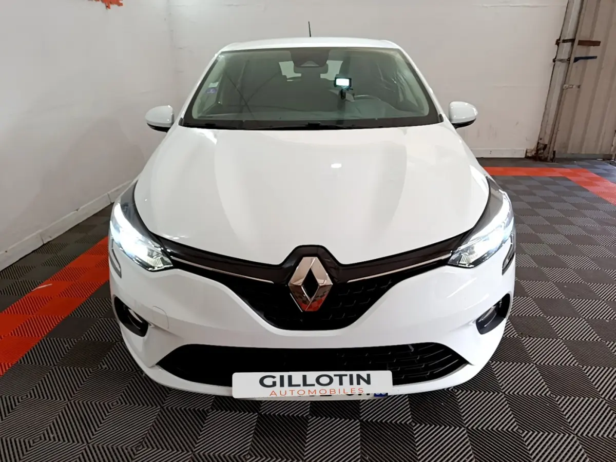 Vue frontale d'une Renault Clio Business blanche avec phares LED allumés sur sol damier noir et rouge.