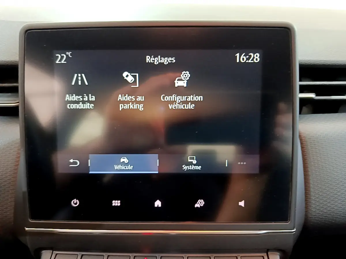 Écran tactile central du tableau de bord de la Renault Clio Business blanc, affichant les réglages d'aides à la conduite et parking.