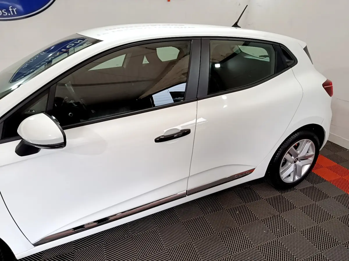 Profil côté gauche d'une Renault Clio Business blanche, avec poignées noires et jantes alliage visibles sur fond intérieur.