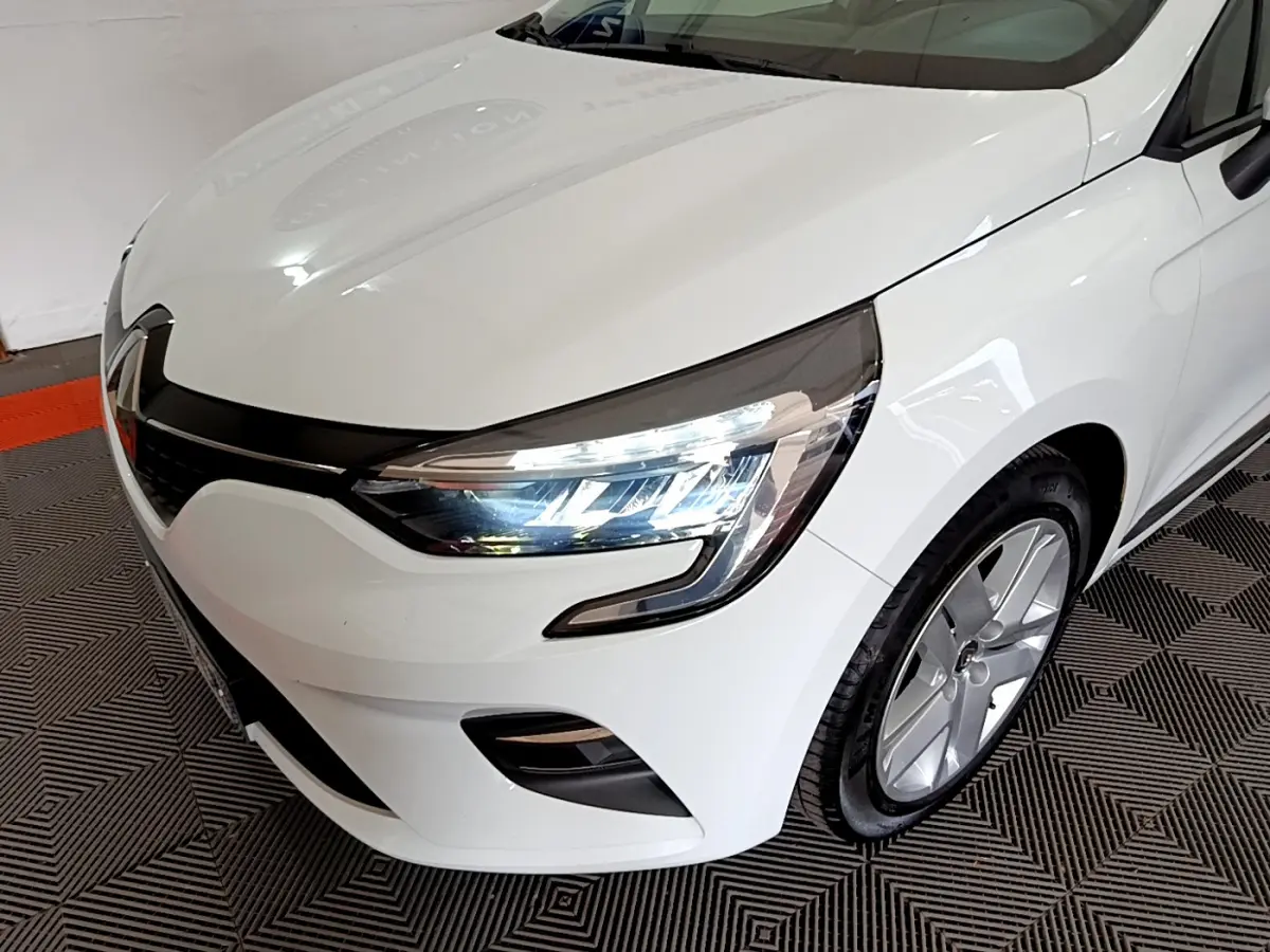 Vue 3/4 avant droit d'une Renault Clio Business blanche mettant en valeur ses phares LED et sa calandre noire brillante.