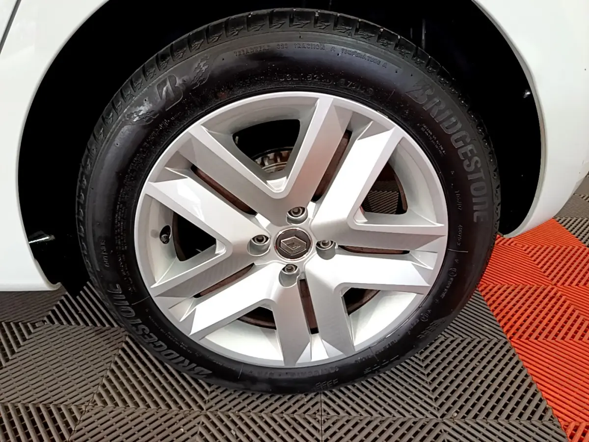 Gros plan sur la roue arrière droite d'une Renault Clio Business blanche, avec pneu Bridgestone visible sur sol carrelé noir et rouge.