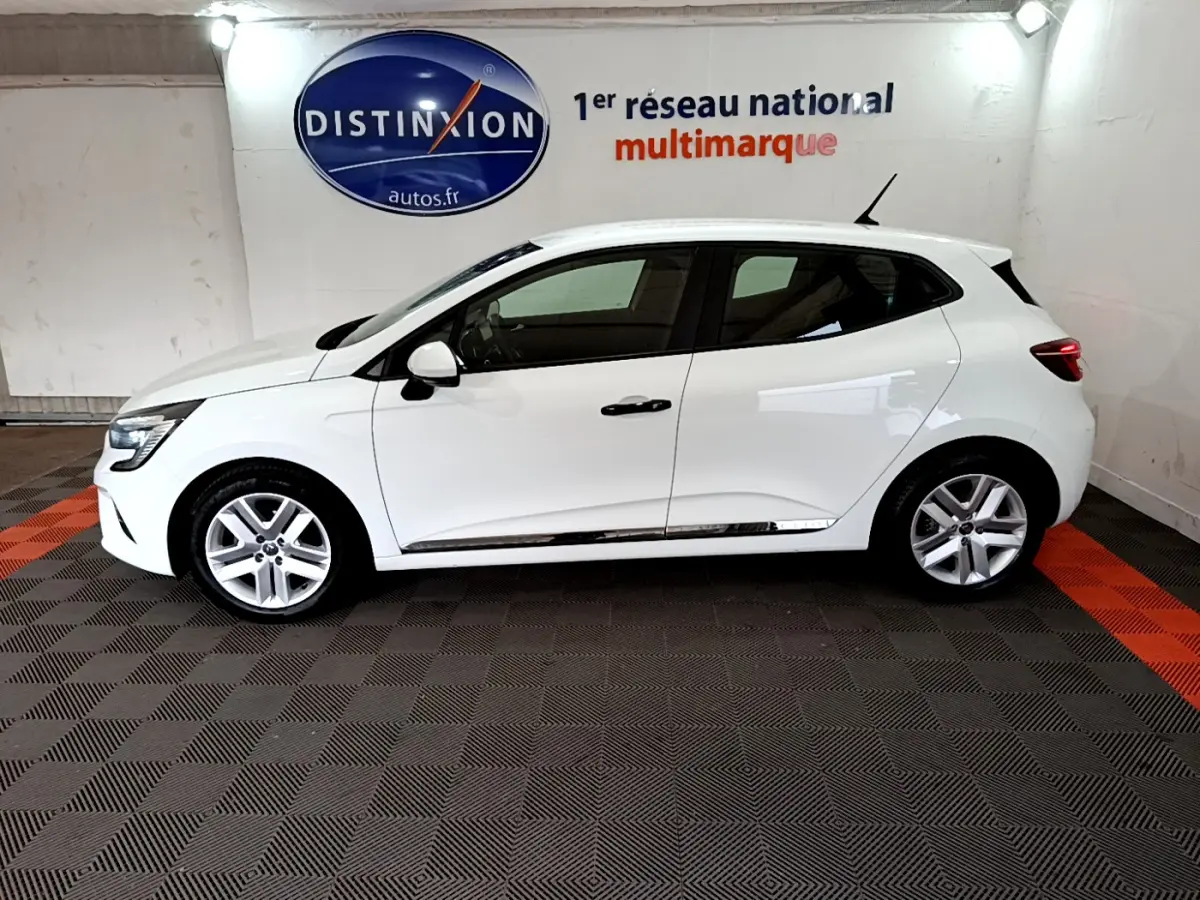 Profil droit d'une Renault Clio Business blanche 2021, avec jantes alliage et poignées noires, en intérieur showroom.