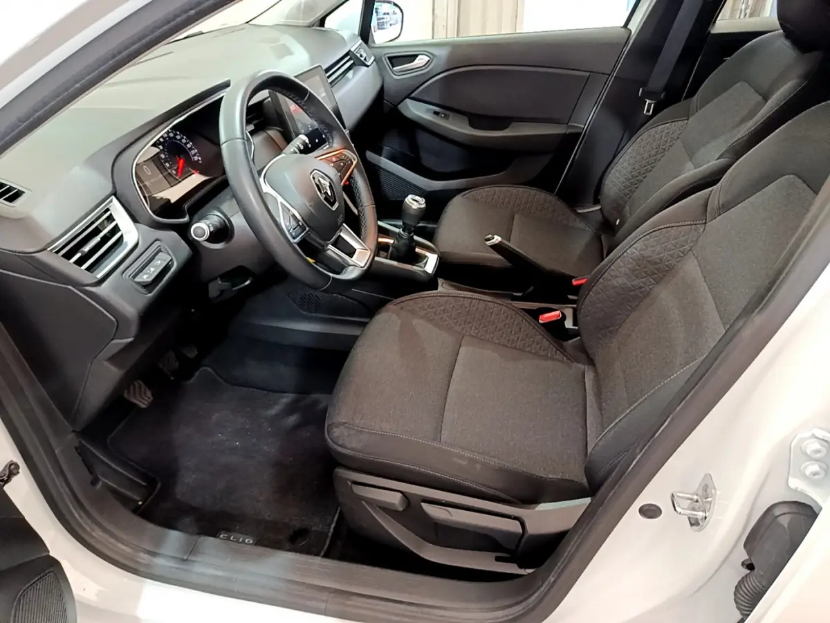 Vue intérieure côté conducteur de la Renault Clio Business blanche, montrant sièges tissu noir et volant cuir multifonctions.