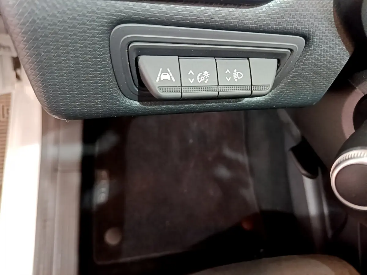 Gros plan sur les commandes d'assistance à la conduite sous le tableau de bord d'une Renault Clio Business blanche.