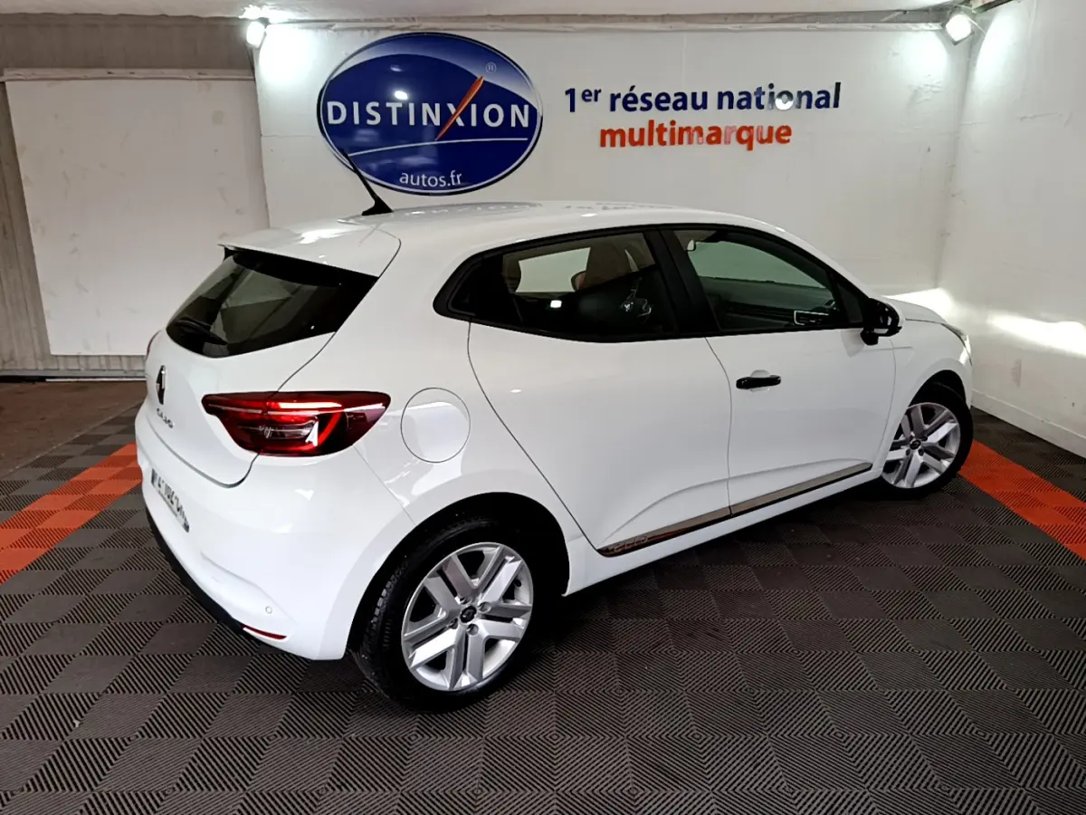 Vue 3/4 arrière droite d'une Renault Clio Business blanche, avec jantes alliage et vitres teintées, en intérieur showroom.