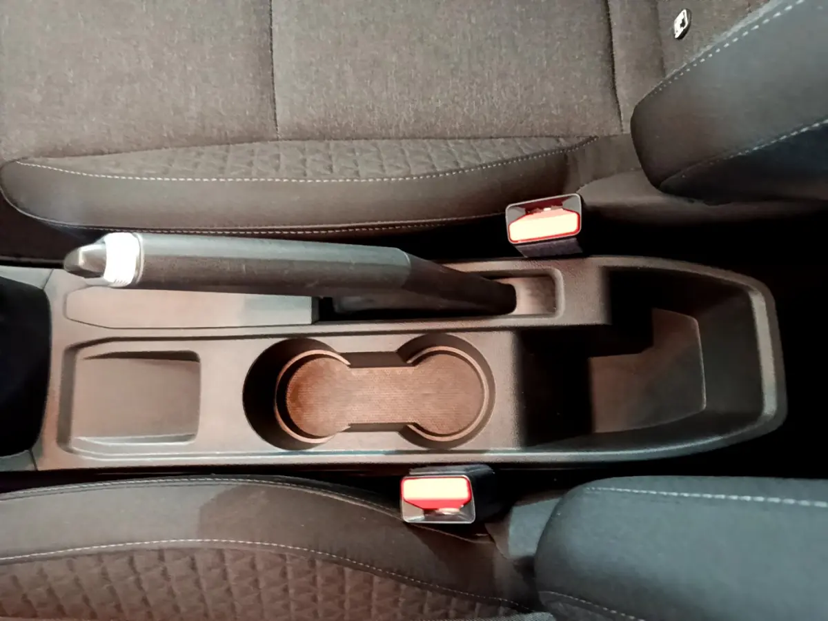 Vue plongeante sur la console centrale noire de la Renault Clio Business avec frein à main manuel et porte-gobelets.