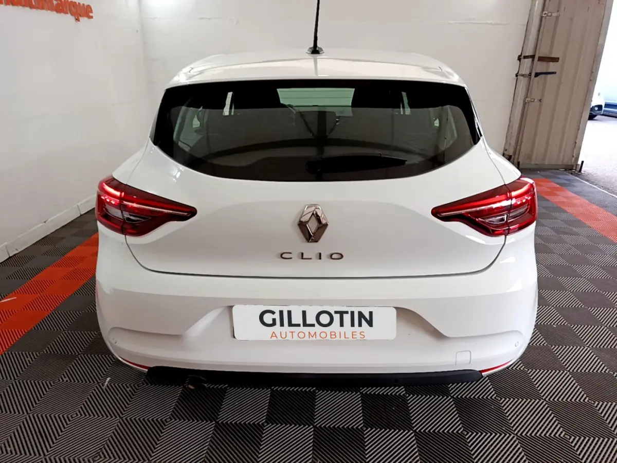 Vue arrière d'une Renault Clio Business blanche 2021 avec feux LED et logo Renault visible sur fond intérieur showroom.