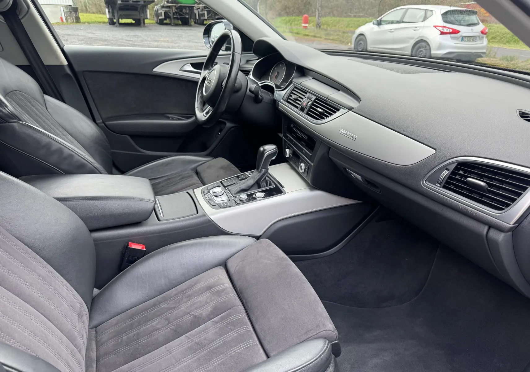 Vue intérieure côté conducteur de l'Audi A6 Avant 2015 avec sièges cuir et alcantara gris, tableau de bord moderne et console centrale.