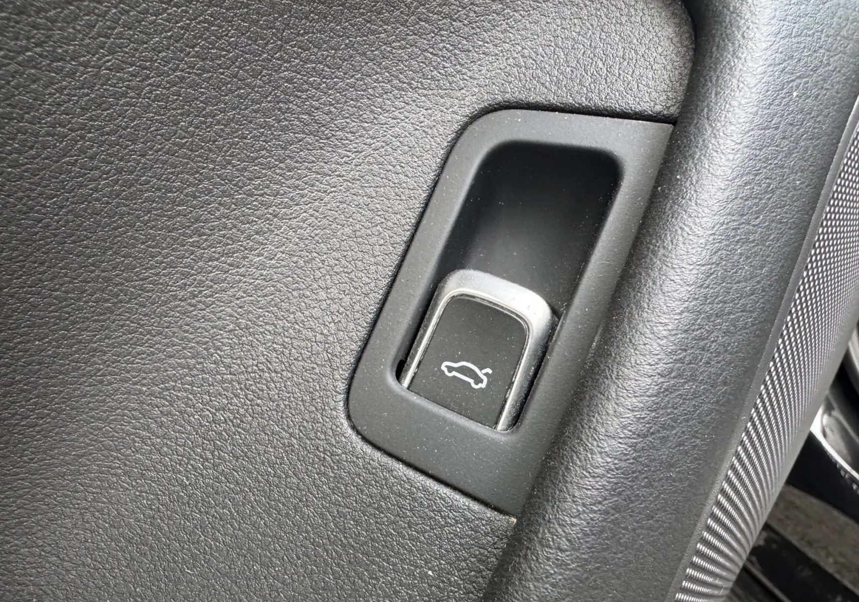 Gros plan sur le bouton d'ouverture du hayon dans l'habitacle noir de l'Audi A6 Avant 2015.