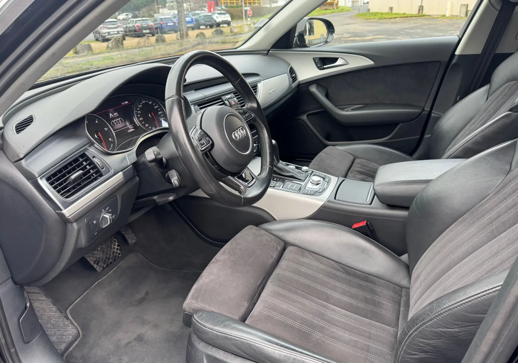 Vue intérieure côté conducteur de l’Audi A6 Avant 2015, sièges cuir noir et tableau de bord moderne avec volant multifonction.