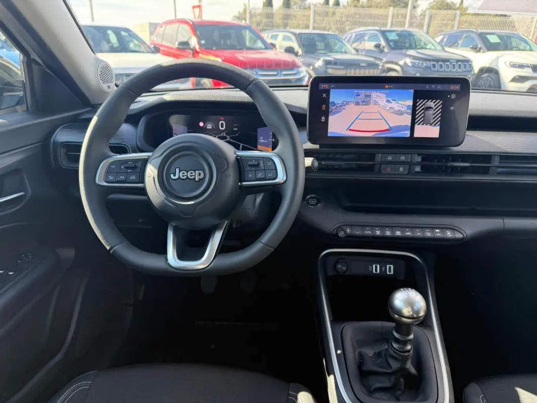 Vue intérieure frontale du Jeep Avenger 2025, tableau de bord noir avec volant multifonction et écran tactile affichant la caméra de recul.