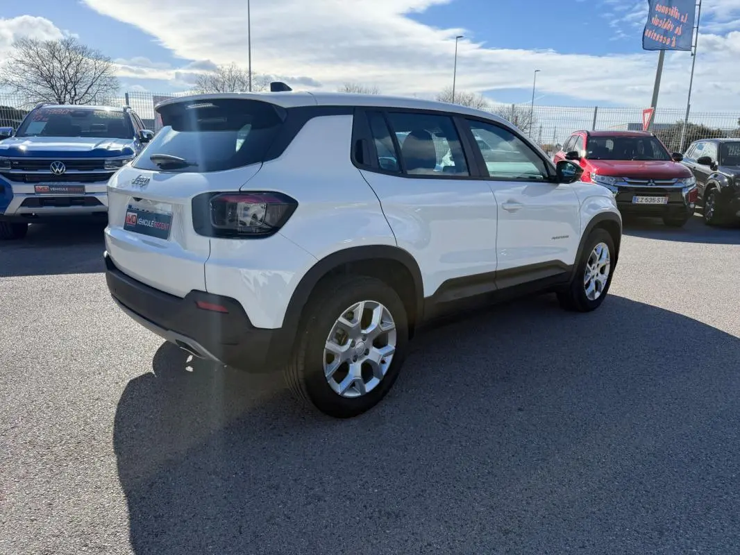 Vue 3/4 arrière droit d’un Jeep Avenger blanc avec jantes alliage 17 pouces, feux arrière fumés et toit noir.