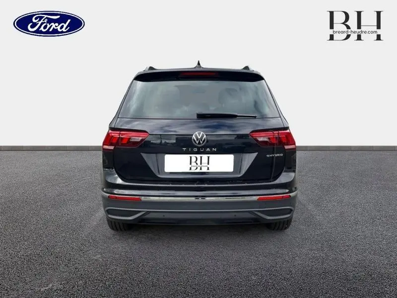 Vue arrière d'un Volkswagen Tiguan noir intense nacré, mettant en valeur les feux LED et le badge hybride sur le hayon.