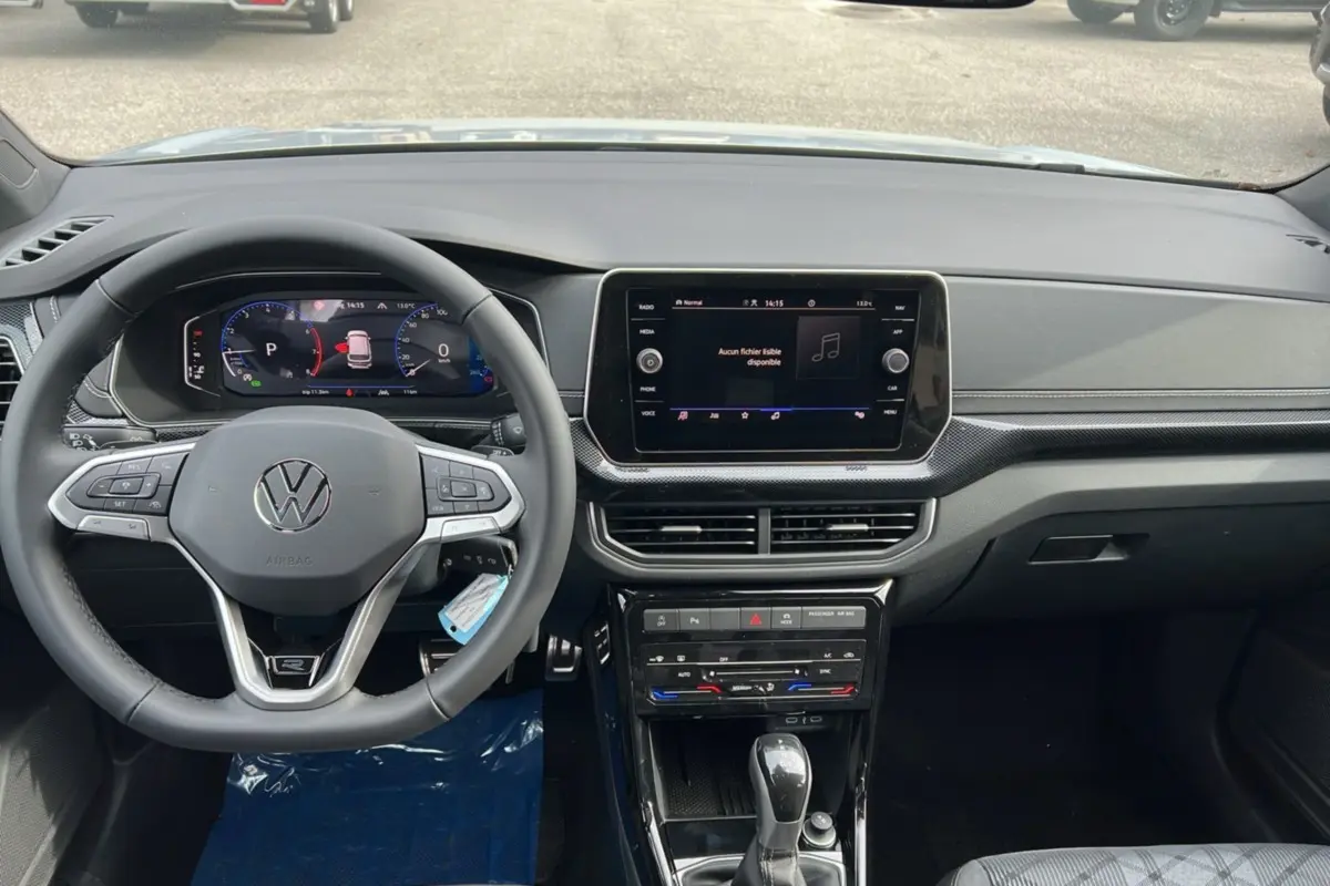 Vue intérieure du tableau de bord du Volkswagen T-Cross gris argent, avec volant multifonctions et écran tactile central.