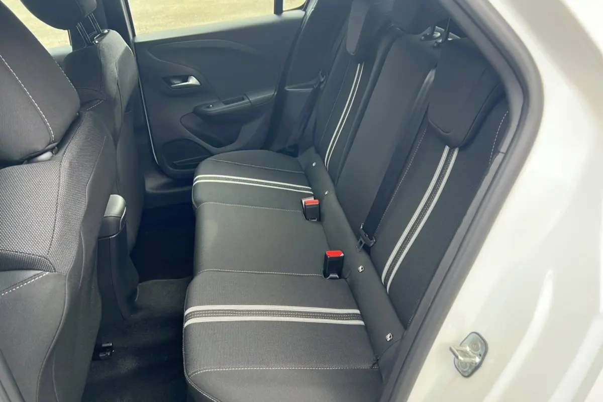 Vue intérieure arrière côté droit de l’Opel Corsa blanc kontur, banquette noire avec bandes grises et ceintures de sécurité.