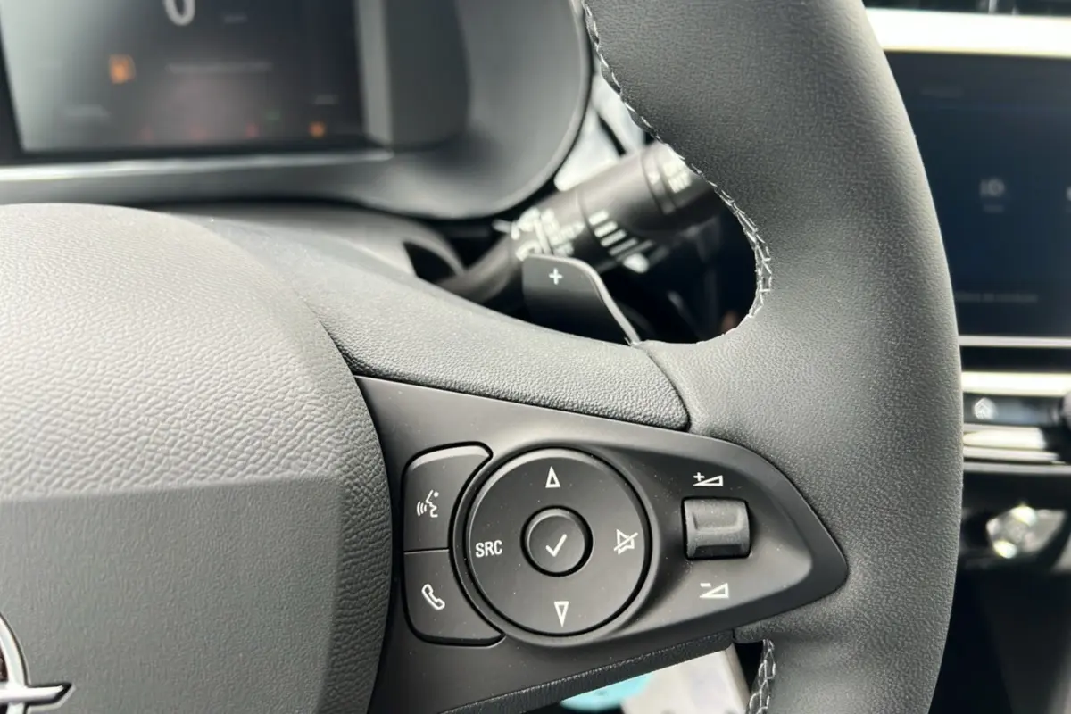 Gros plan sur les commandes multifonctions noires du volant cuir d’une Opel Corsa blanc kontur, version hybride 2026.