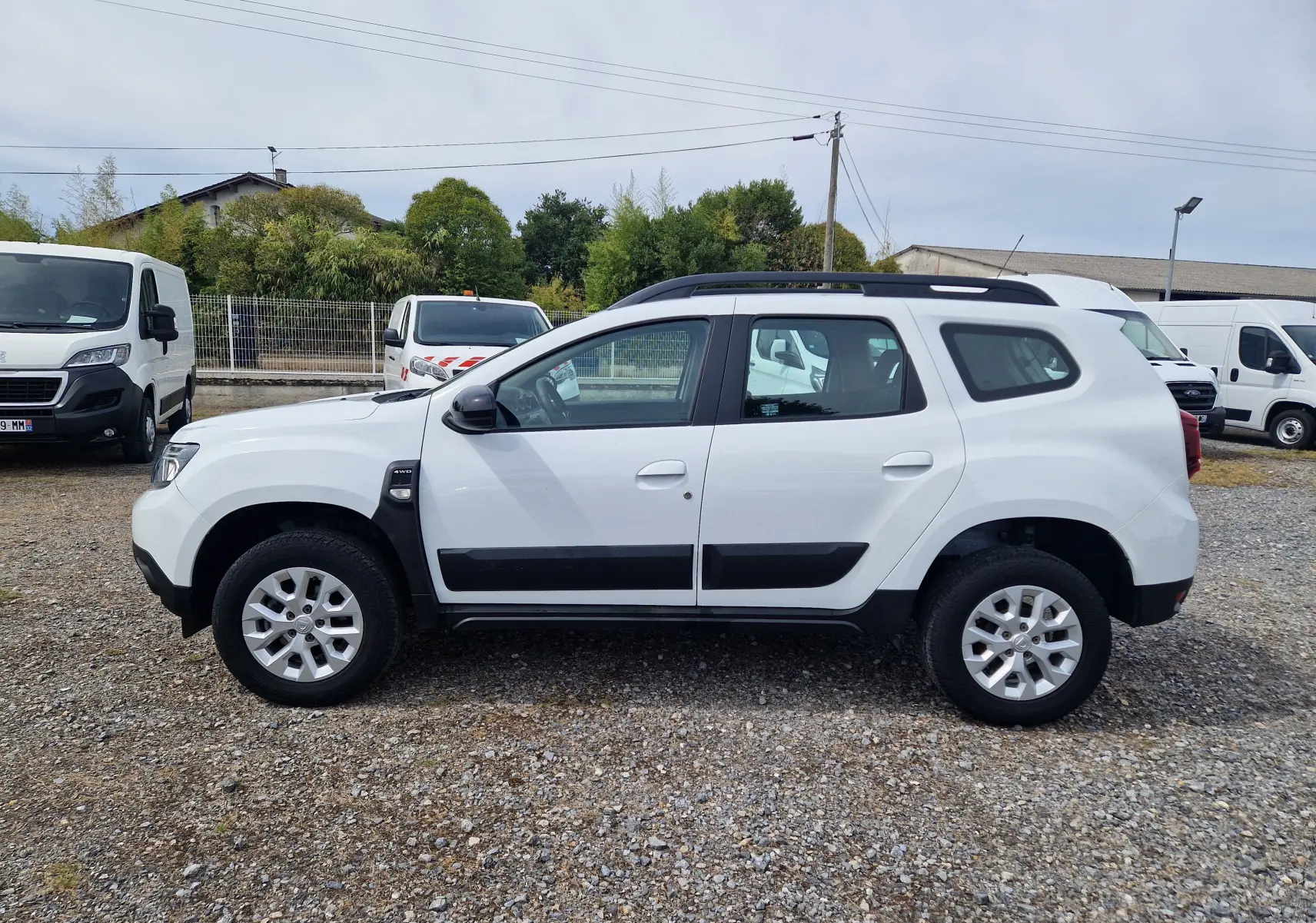 Profil côté gauche d'un Dacia Duster blanc 4x4 2022 avec protections noires et jantes alliage 16 pouces.