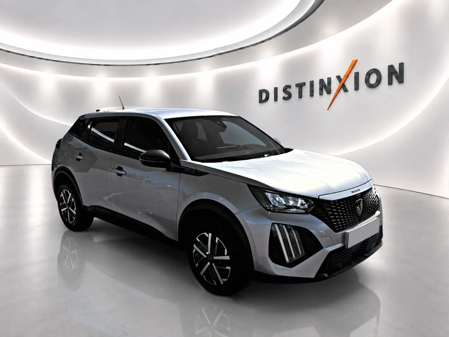 Peugeot 2008 gris 3/4 avant droit en intérieur, avec calandre noire et jantes stylisées noires et argentées.