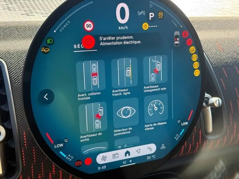 Affichage numérique circulaire du tableau de bord du MINI Countryman argenté, montrant les alertes de sécurité et la température extérieure.